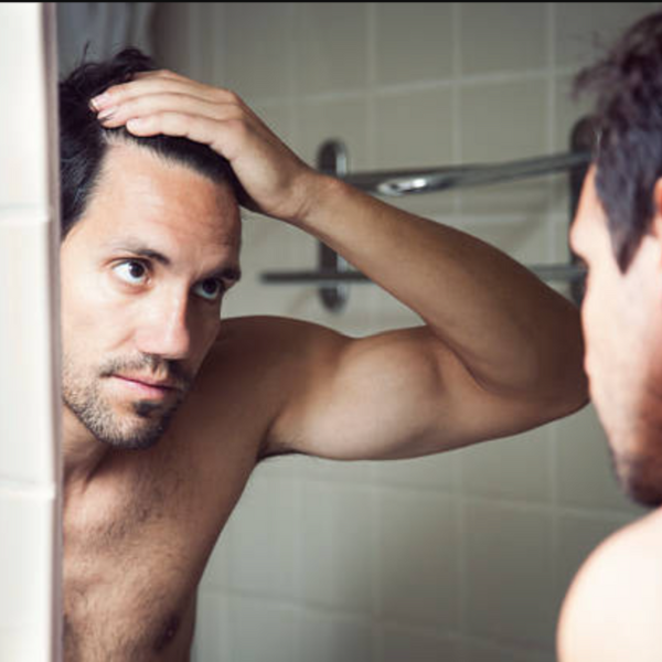 Close-up van een man die in de spiegel kijkt vanwege haaruitval bij mannen